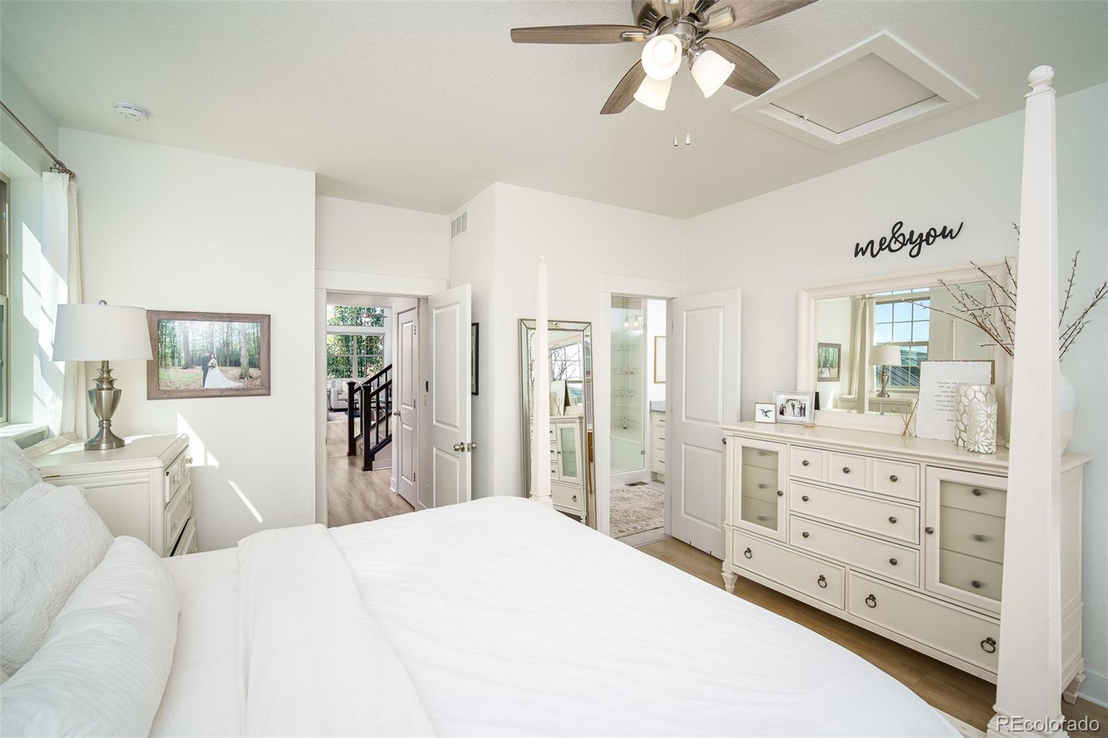 Bright white bedroom with a large bed, matching dressers, ceiling fan, and open bathroom doorway.