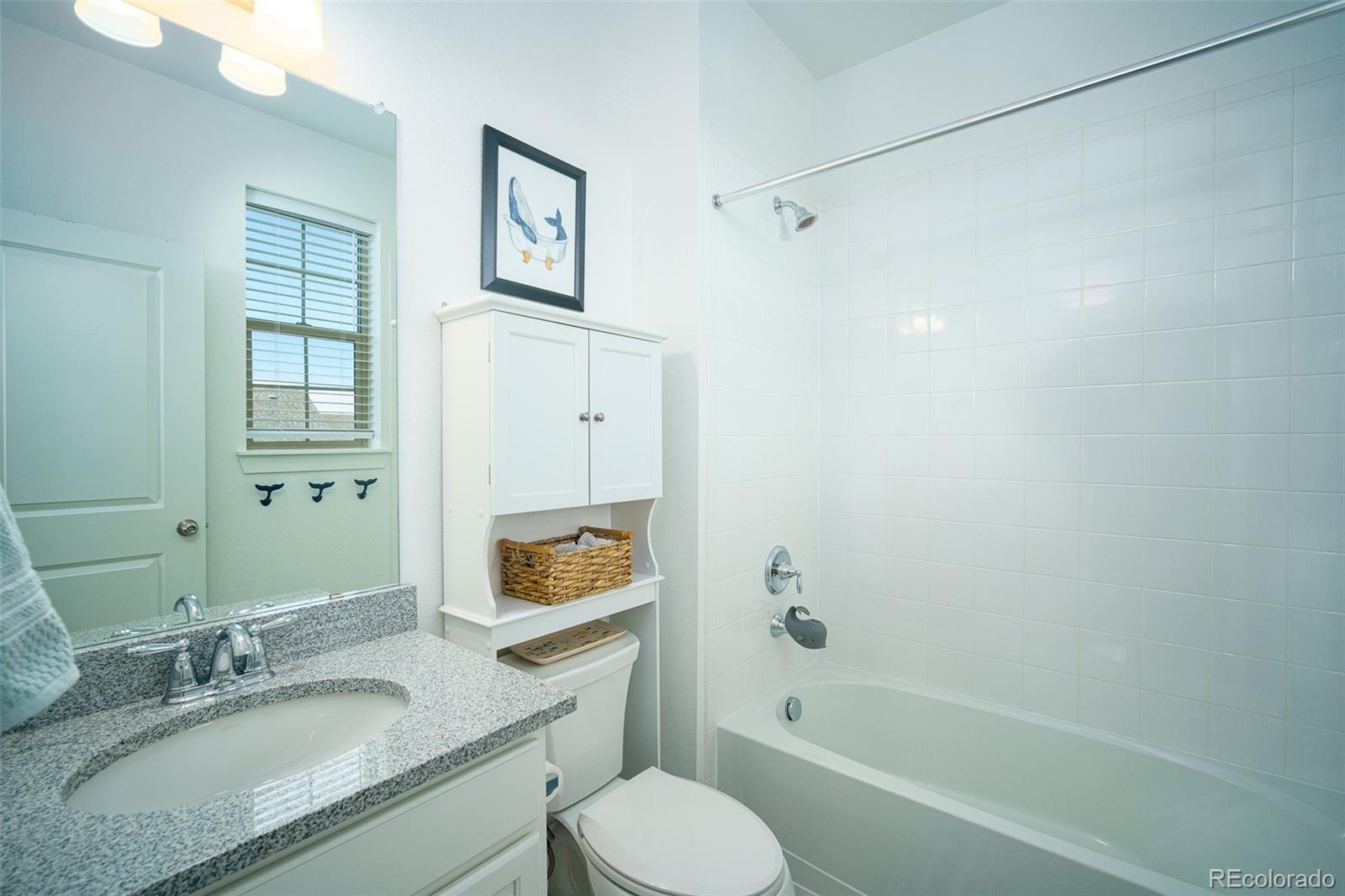 Bright bathroom with a granite vanity, white cabinetry, and a tiled tub-shower.