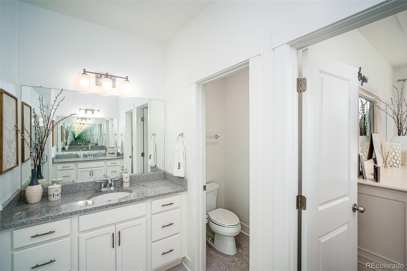 Bathroom with a white vanity, speckled countertop, large mirrors, and a separate toilet area.