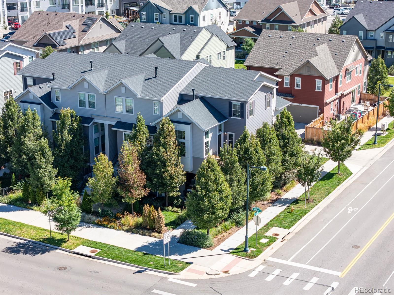 Gray townhomes at a landscaped street corner, viewed from above with a crosswalk nearby.