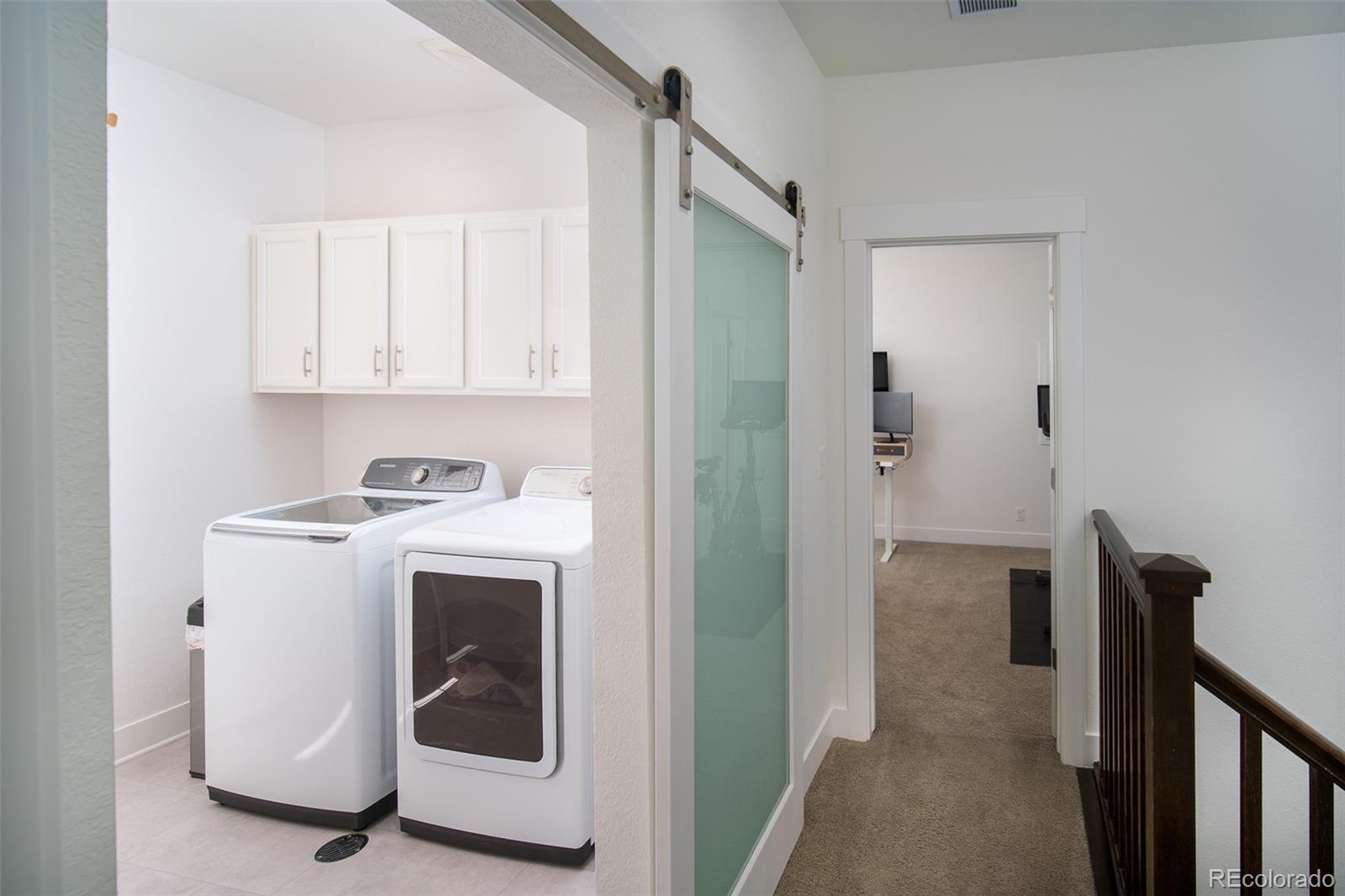 Laundry room with white washer and dryer, frosted-glass sliding door, and adjacent carpeted hallway.