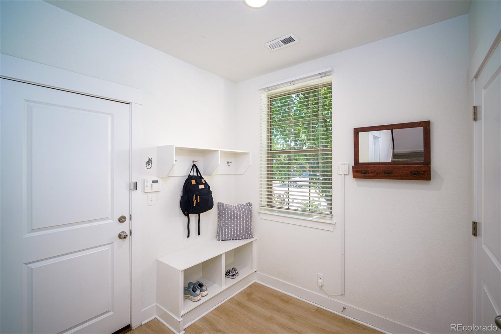 Bright entryway with a shoe bench, wall hooks, and a window overlooking greenery.