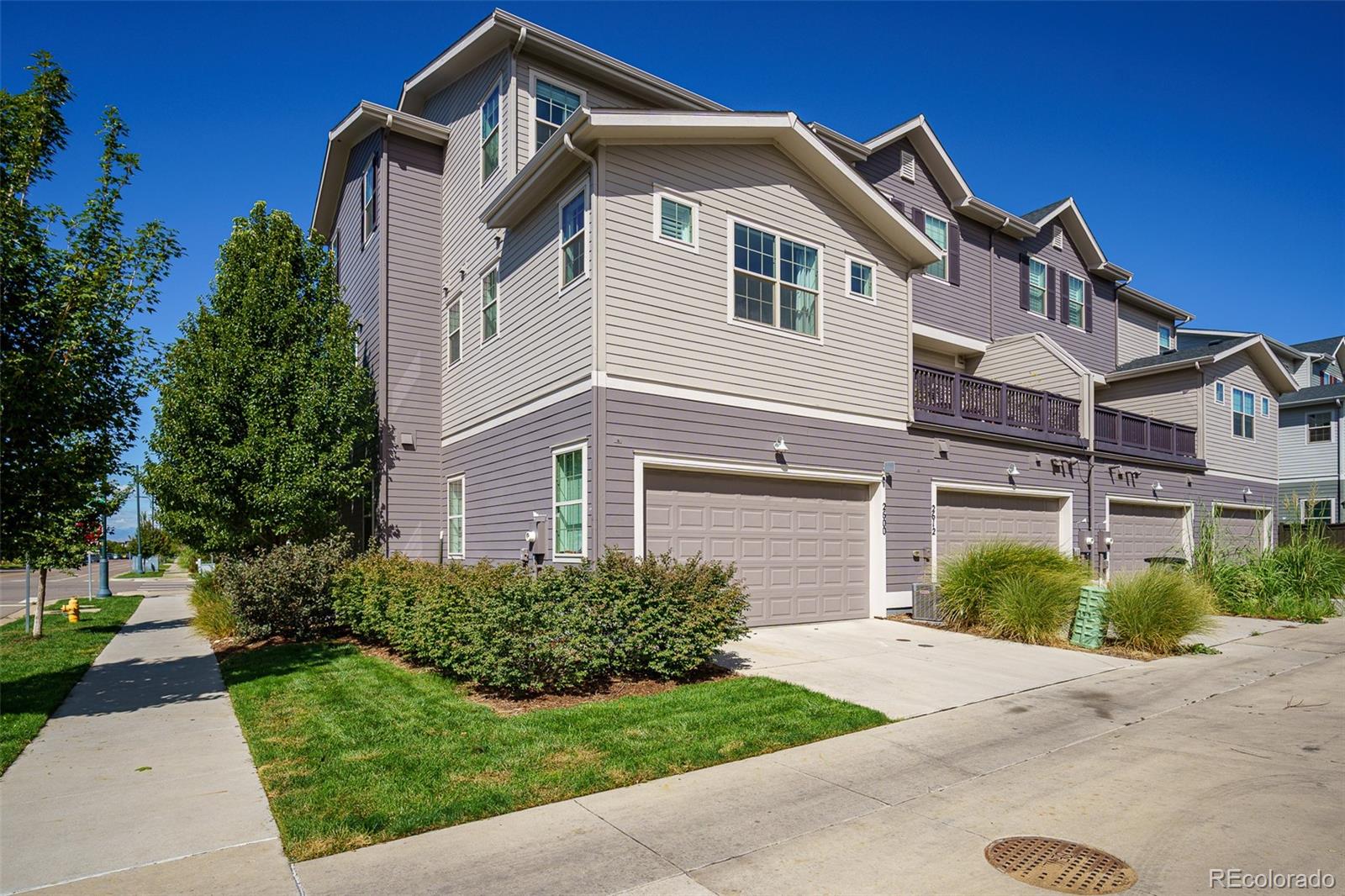 Multi-story townhome with attached garages, a raised deck, and landscaped lawn.