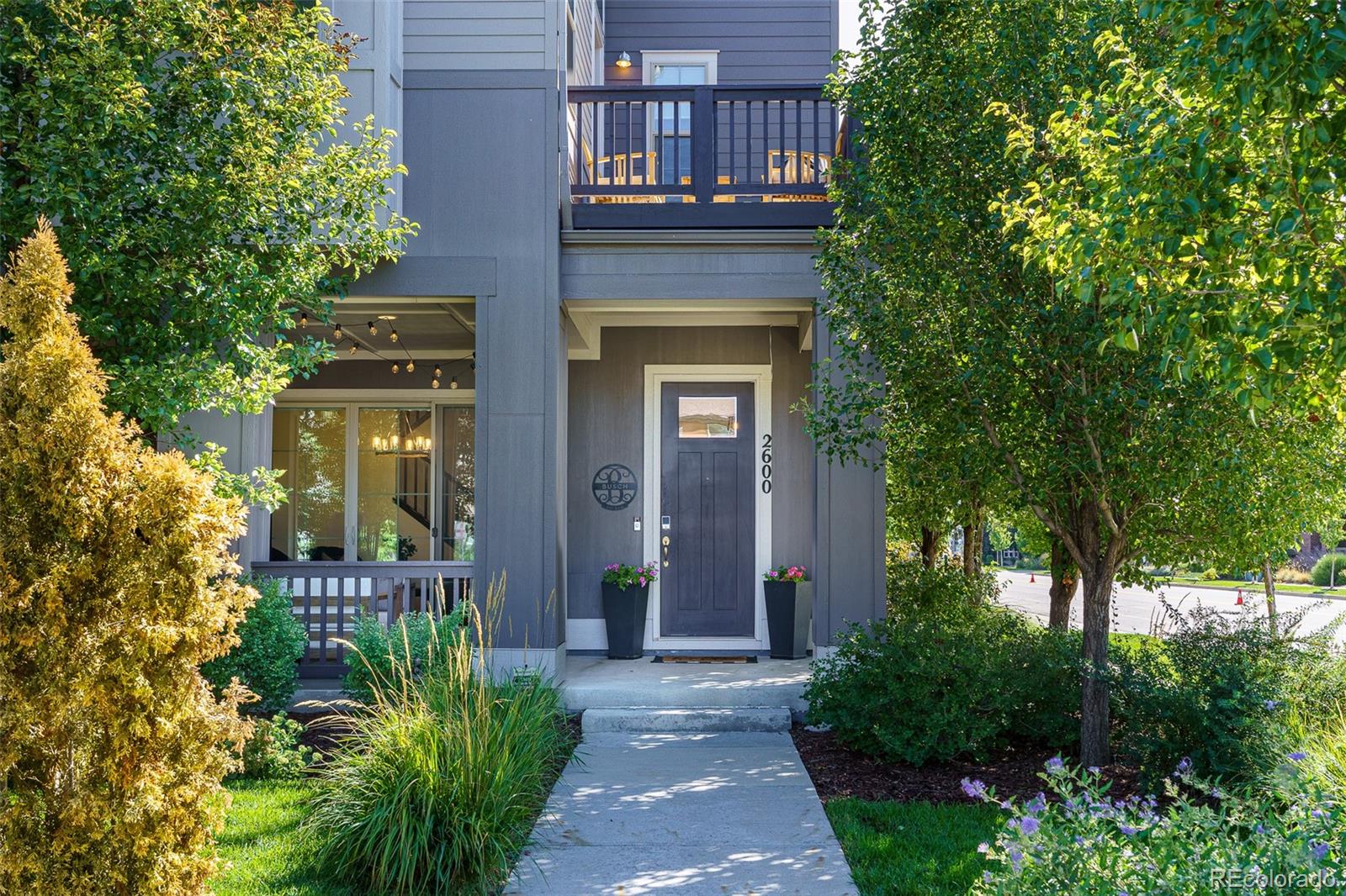 Gray home entrance with a covered porch, upper balcony, and landscaped walkway.