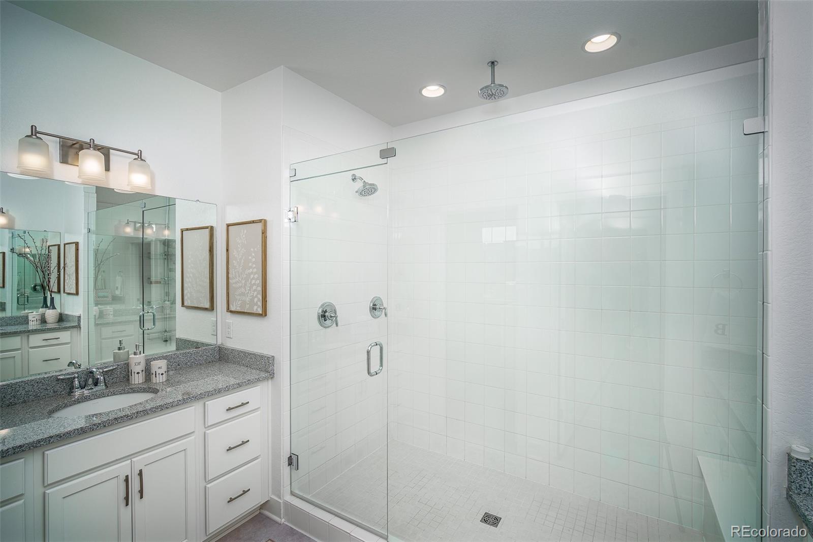 Bathroom with a spacious glass-enclosed, white-tiled walk-in shower beside a white vanity.