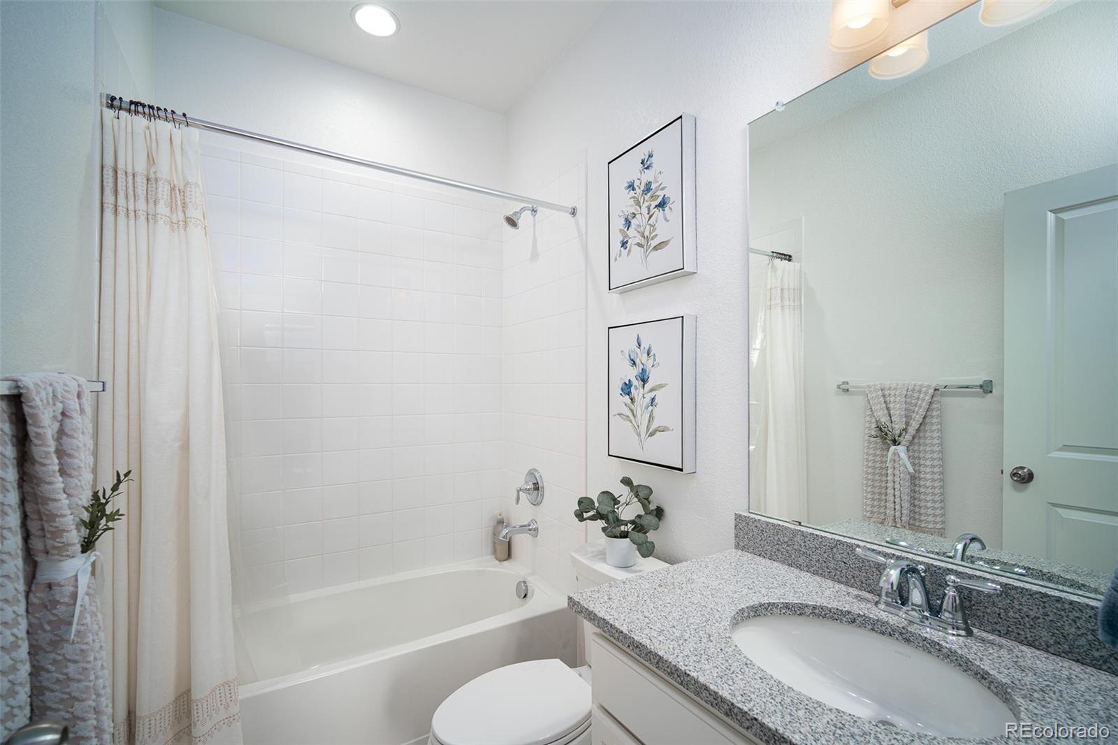 Bathroom with a tiled tub and shower, granite vanity, large mirror, and framed floral prints.