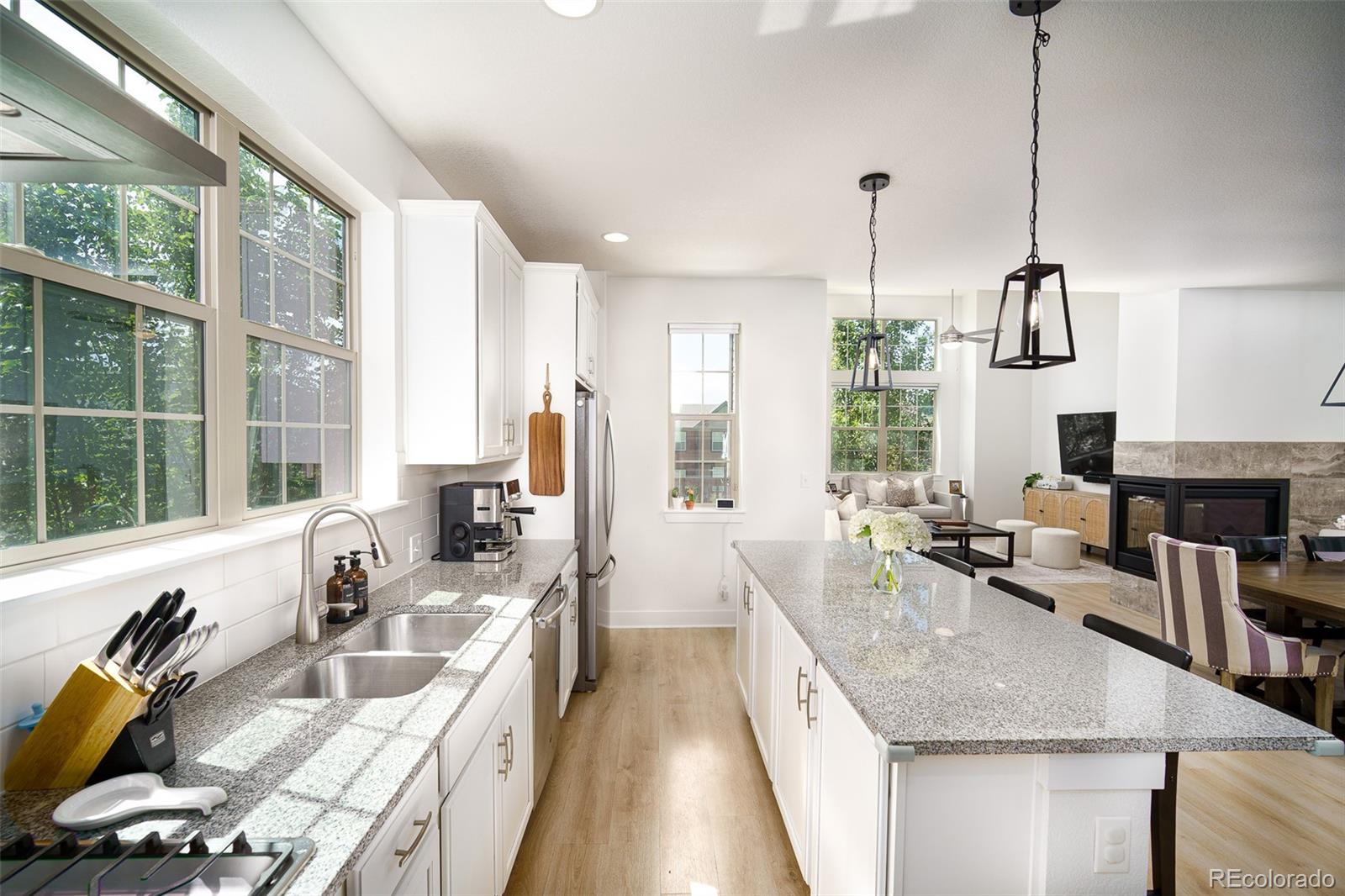 Bright kitchen with a large granite island opening to a furnished living room and fireplace.