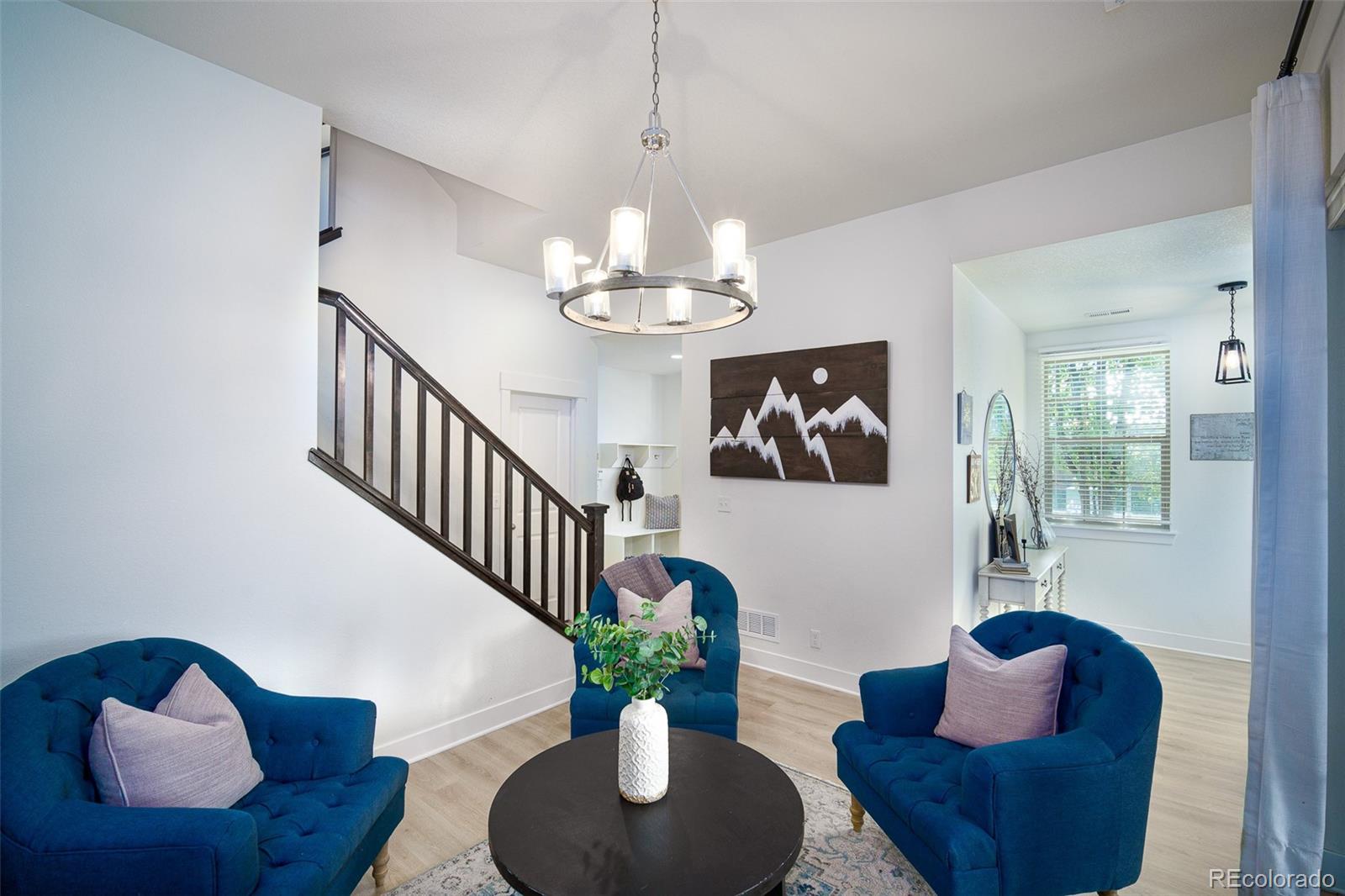 Living room with blue tufted chairs, a dark wood staircase, and a round coffee table.