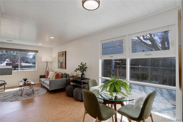 Living and dining area with large windows, a gray sofa, and a round table.