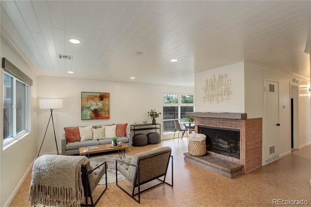 Furnished living room with a brick fireplace, neutral seating, and large windows.