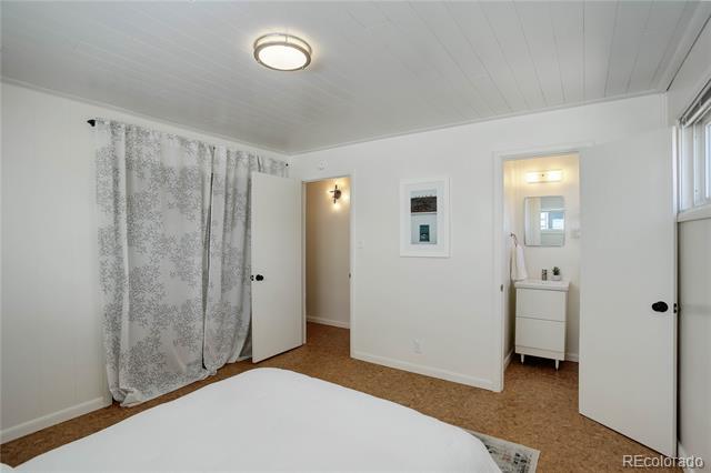 Bedroom with brown carpet, a paneled ceiling, and open doorways to a bathroom and hallway.