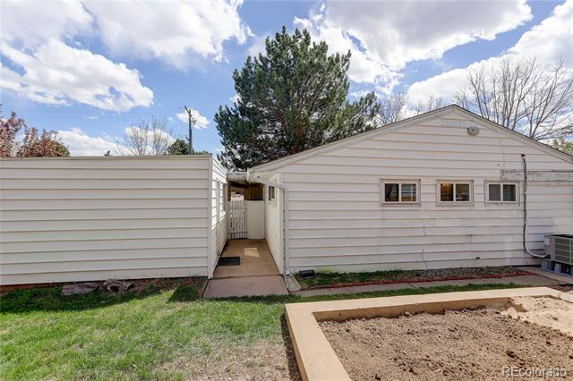 Rear exterior of a white-sided home with a narrow walkway and raised garden bed.