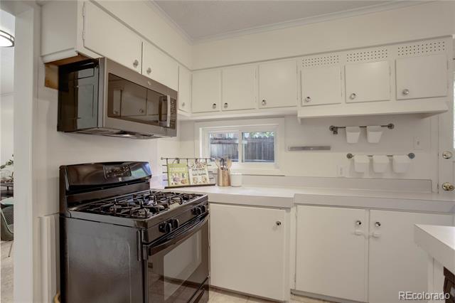 White kitchen with a black gas range and microwave beneath white cabinets.
