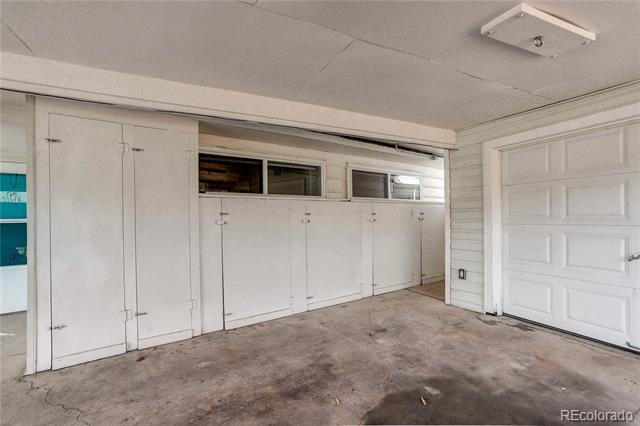 Vacant garage with built-in white cabinets, a white garage door, and a stained concrete floor.
