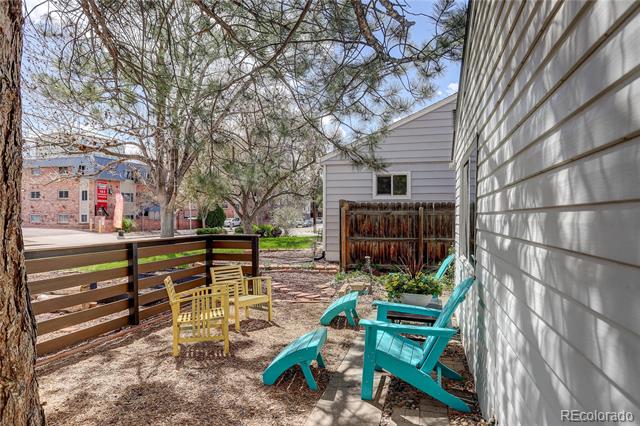 Side patio with colorful outdoor chairs beside white house siding and a wooden fence.