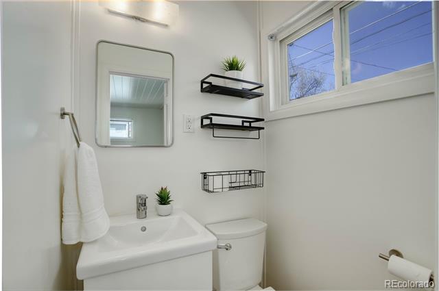 Bathroom with a white sink and toilet, black wall shelves, and a high window.