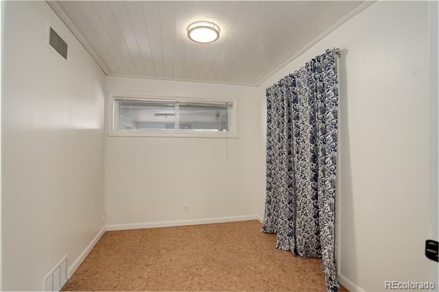 Unfurnished room with tan carpet, a narrow window, patterned curtains, and a ceiling light.