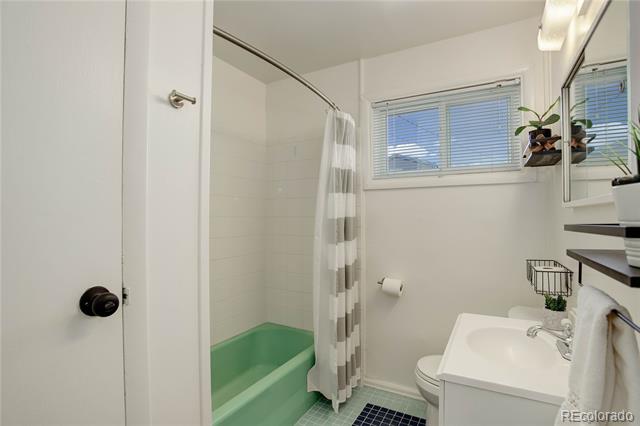 Bathroom with mint-green bathtub, striped shower curtain, and white vanity beneath a window.