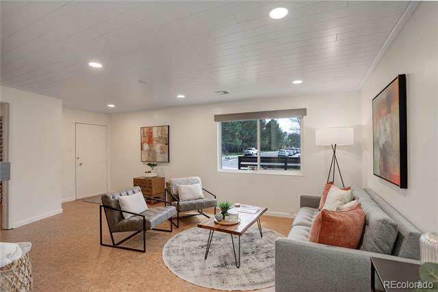 Staged living room with a gray sofa, two accent chairs, and a large window overlooking trees.
