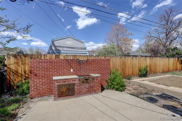 Backyard patio with a red brick outdoor fireplace beside a wooden privacy fence.