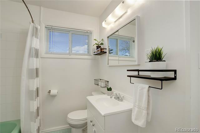 Bathroom with a white vanity, toilet, curtained bathtub, and windows with blinds.