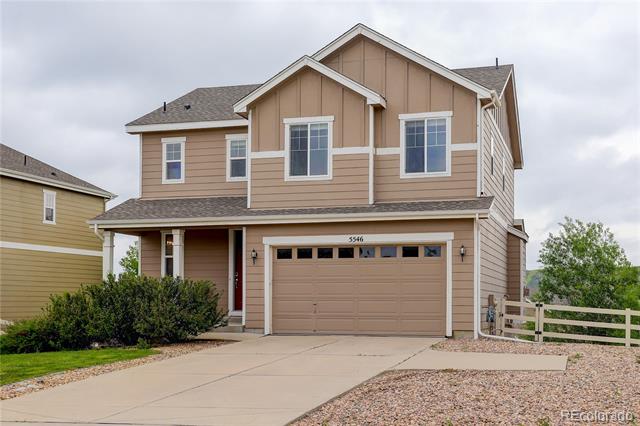 Two-story tan house with a two-car garage, covered entry, and wide concrete driveway.