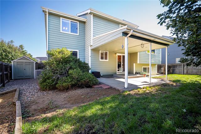 Two-story home's rear exterior with a covered patio, backyard lawn, and storage shed.