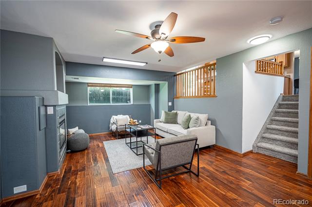 Basement living room with a white sofa, dark wood floors, and carpeted stairs.