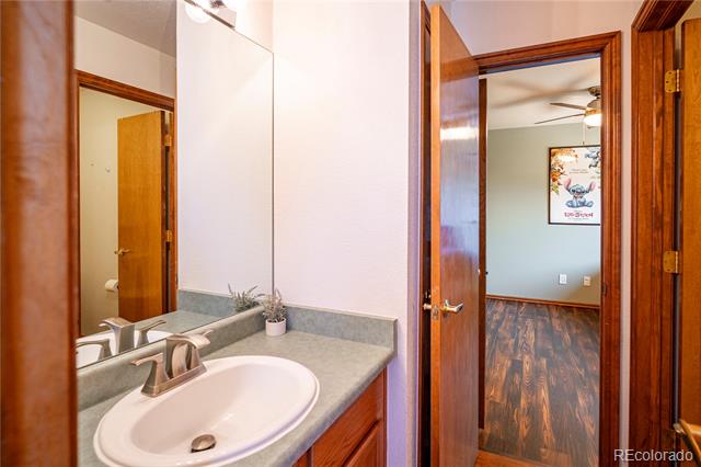Bathroom vanity with an oval sink and gray countertop beside an open doorway to a wood-floored room.