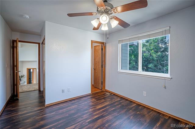 Empty bedroom with dark hardwood floors, a ceiling fan, and a window overlooking trees.