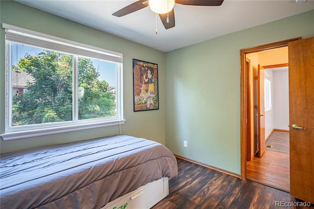 Bedroom with a bed beneath a wide window overlooking leafy trees and an open doorway to the hall.