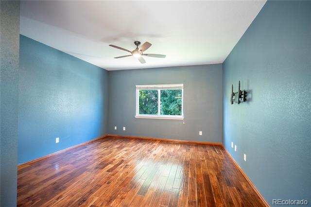 Empty blue bedroom with polished hardwood floors, ceiling fan, and a window overlooking greenery.