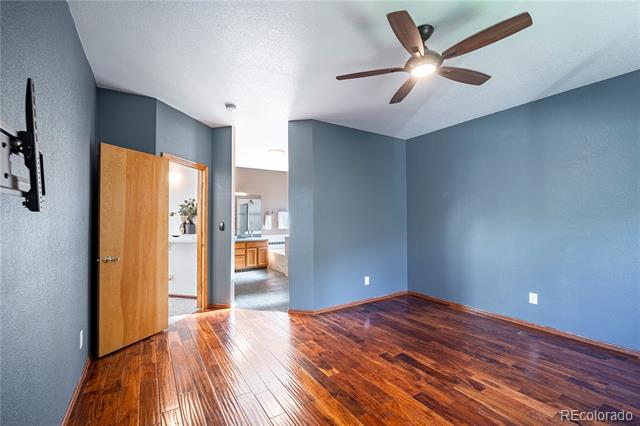 Empty blue-gray room with polished hardwood floors and a ceiling fan, viewed toward an open doorway.