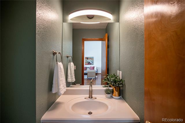 Bathroom vanity with an oval sink, chrome faucet, and potted plants beside the mirror.