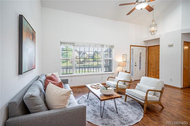 Furnished living room with vaulted ceiling, hardwood floors, and large windows overlooking greenery.