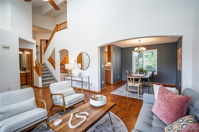 Living and dining room with hardwood floors, a wood-railed staircase, and a chandelier over the dining table.