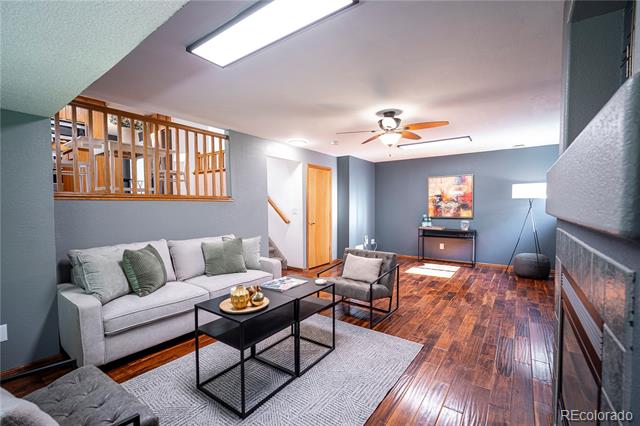Living room with a gray sectional, dark wood floors, ceiling fan, and fireplace.
