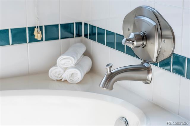 Bathtub with brushed-metal fixtures, teal tile accents, and rolled white towels.