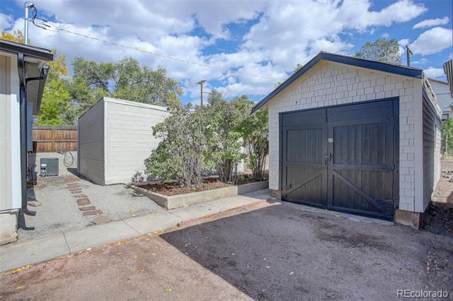 Paved driveway with a white garage with dark double doors and a smaller shed.