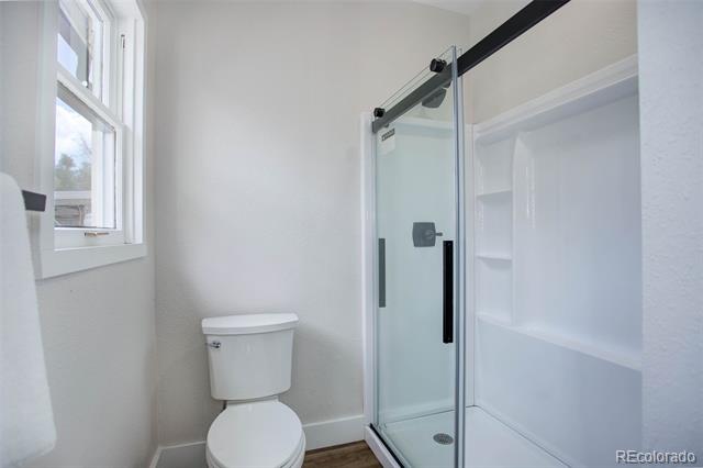 Bathroom with a glass shower enclosure, built-in shelves, toilet, and tall window.
