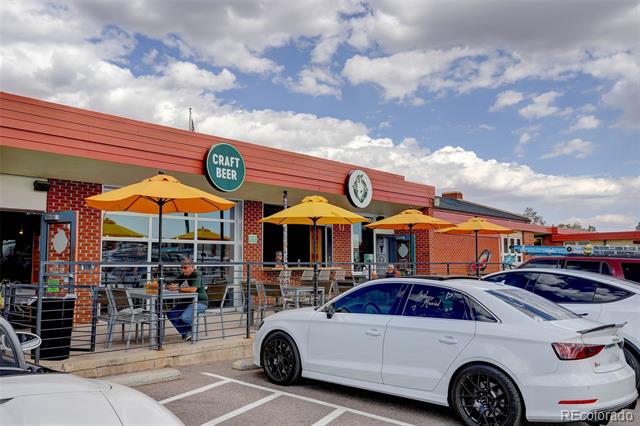 Brick commercial storefront with a red awning, patio seating, and orange umbrellas beside parked cars.