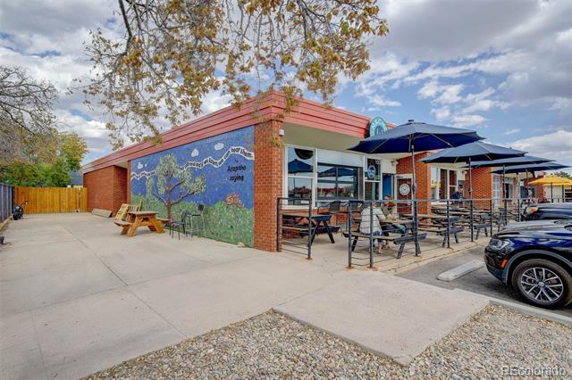 Brick commercial building with a colorful mural and outdoor patio shaded by blue umbrellas.