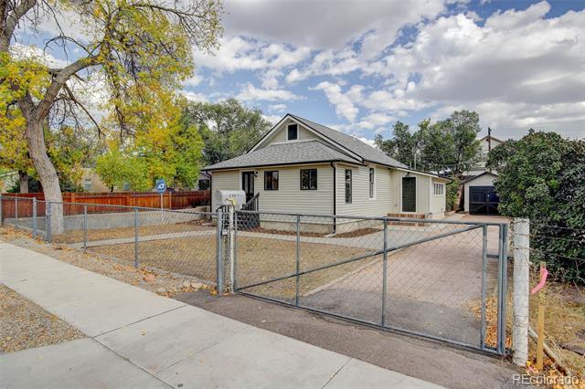 Single-story house behind a chain-link fence, with a paved driveway and detached garage.