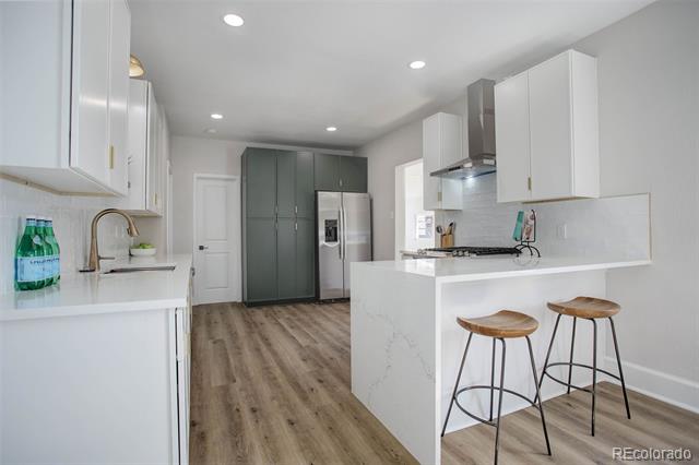 Modern kitchen with white cabinets, dark green pantry cabinetry, marble-look island, and two wooden bar stools.