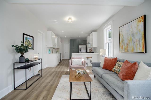 Open-plan living room with a gray sofa, colorful cushions, and a kitchen breakfast bar.