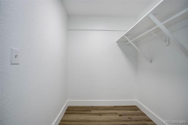 Empty closet with a white shelf and hanging rod above wood-look flooring.