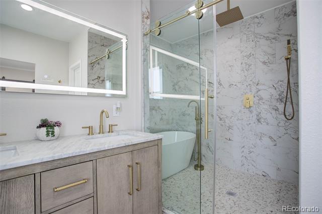 Bathroom with a marble vanity, brass fixtures, freestanding tub, and glass-enclosed shower.