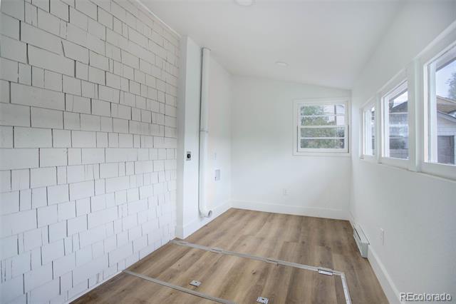 Bright narrow room with wood-look floors, a white brick accent wall, and windows along one side.