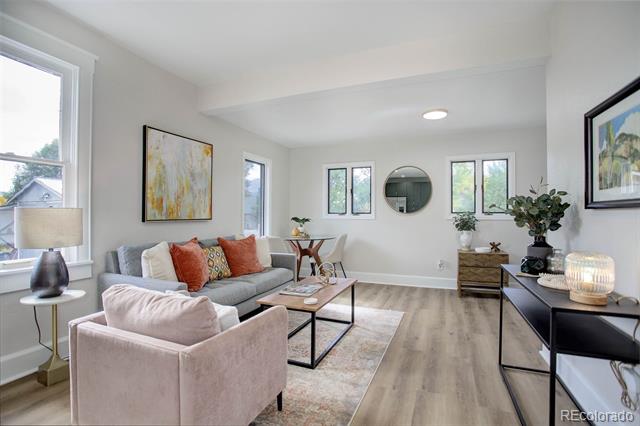 Staged living room with a gray sofa, pink armchair, and large windows.