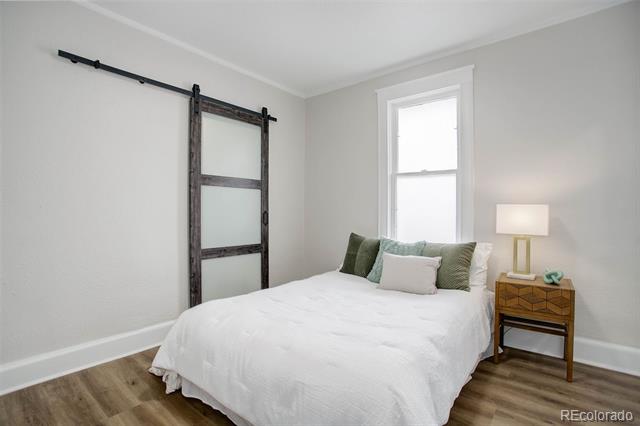 Staged bedroom with a white bed, green accent pillows, and a dark sliding barn door.